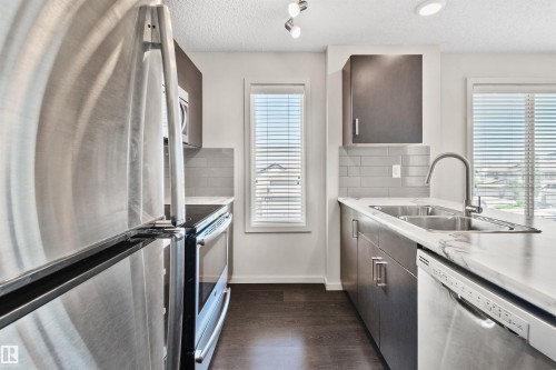 Stainless steel appliances, dark wood-finish cabinetry, light marble-look countertops, subway tile backsplash, and dark wood-finish flooring - #318 5521 7 Av Sw Sw, Edmonton, AB - Indoor Photo Showing Kitchen With Stainless Steel Kitchen With Double Sink With Upgraded Kitchen
