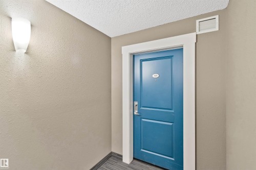 Blue panel door with white trim, wall-mounted light fixture, and textured walls - #318 5521 7 Av Sw Sw, Edmonton, AB -  Photo Showing Other Room