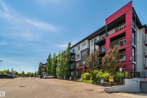 Multi-story building featuring modern red and gray exterior paneling, private balconies, and a paved parking lot with designated spaces - #318 5521 7 Av Sw Sw, Edmonton, AB - Outdoor