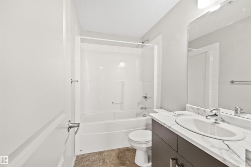 Bathroom featuring a white bathtub, shower with glass enclosure, single vanity with oval sink, stone-finish countertop, and dark wood-finish cabinetry - #318 5521 7 Av Sw Sw, Edmonton, AB - Indoor Photo Showing Bathroom