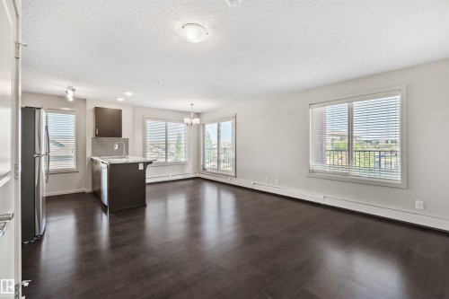 Open-concept living space with dark wood-finish flooring, white walls, and multiple windows - #318 5521 7 Av Sw Sw, Edmonton, AB - Indoor Photo Showing Kitchen