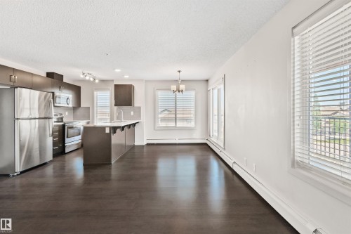 Open-concept living area with dark wood-finish flooring, a kitchen island, and stainless steel appliances - #318 5521 7 Av Sw Sw, Edmonton, AB - Indoor Photo Showing Kitchen With Stainless Steel Kitchen