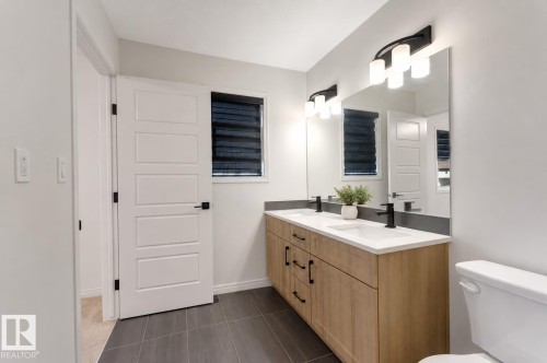 Double vanity with wood-finish cabinetry, white countertops, matte black faucets, and an expansive mirror - 1263 Watt Drive Sw, Edmonton, AB - Indoor Photo Showing Bathroom
