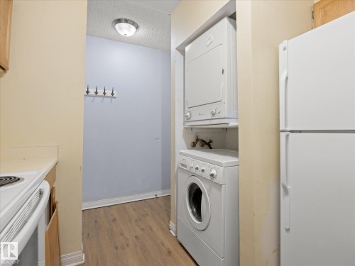 Integrated stackable washer and dryer, wood-finish flooring, included refrigerator, overhead flush-mount lighting, and wall-mounted coat rack - #110 10139 117 St Nw, Edmonton, AB - Indoor Photo Showing Laundry Room