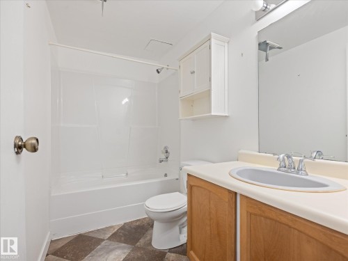 Bathroom featuring a shower-tub combination, wood-finish vanity with an integrated sink, wall-mounted mirror, overhead lighting, and checkerboard floor tiles - #110 10139 117 St Nw, Edmonton, AB - Indoor Photo Showing Bathroom