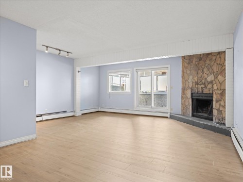 Wood-finish flooring, stone-clad fireplace, track lighting, and sliding glass door - #110 10139 117 St Nw, Edmonton, AB - Indoor Photo Showing Living Room With Fireplace