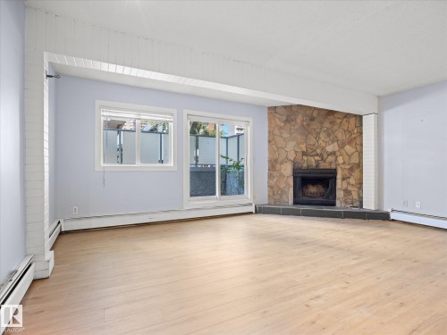 Wood-finish flooring, stone-clad fireplace with hearth, and sliding glass door leading to an outdoor area - #110 10139 117 St Nw, Edmonton, AB - Indoor Photo Showing Living Room With Fireplace