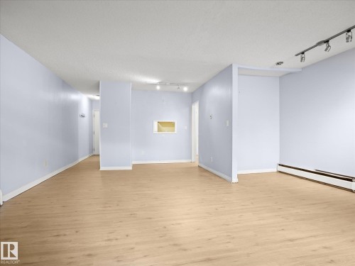 Wood-finish flooring throughout, light blue wall paint, track lighting, and a wall cutout - #110 10139 117 St Nw, Edmonton, AB - Indoor Photo Showing Other Room