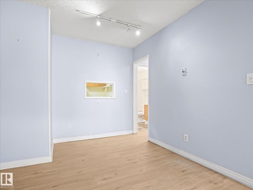 Wood-finish flooring with white baseboards, track lighting, and a pass-through window - #110 10139 117 St Nw, Edmonton, AB - Indoor Photo Showing Other Room