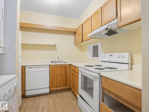 Kitchen featuring wood-finish cabinetry, white appliances, and a stainless steel sink - #110 10139 117 St Nw, Edmonton, AB - Indoor Photo Showing Kitchen