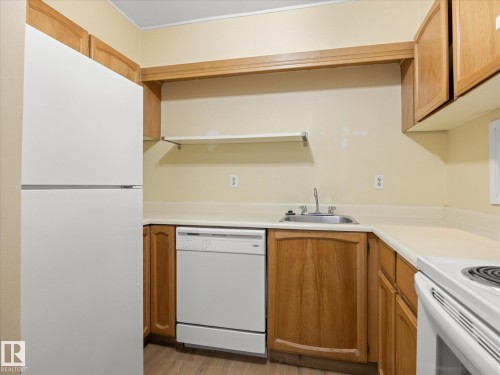 Kitchen featuring wood cabinetry, white appliances, laminate countertops, and wood-finish flooring - #110 10139 117 St Nw, Edmonton, AB - Indoor Photo Showing Kitchen