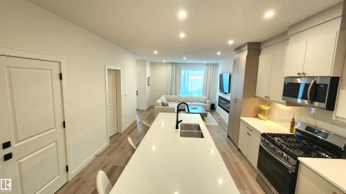 Open-concept living area with wood-finish flooring, recessed lighting, and a kitchen island featuring a double basin sink with a matte black faucet - 220 28 Street Sw, Edmonton, AB - Indoor Photo Showing Kitchen