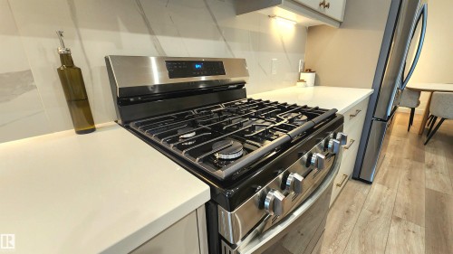 Stainless steel gas range, light-toned countertops, white tiled backsplash, under-cabinet lighting, and wood-finish flooring - 220 28 Street Sw, Edmonton, AB - Indoor Photo Showing Kitchen With Upgraded Kitchen