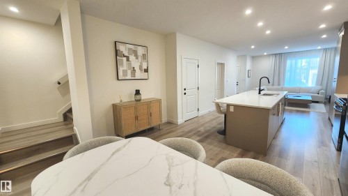 Open-concept living space with wood-finish flooring, a kitchen island with seating, recessed lighting, and a modern staircase with a handrail - 220 28 Street Sw, Edmonton, AB - Indoor