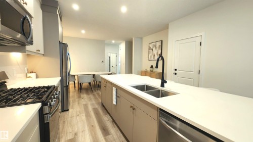 Modern kitchen featuring a large center island with a double basin sink, stainless steel appliances, light wood-finish flooring, and recessed lighting - 220 28 Street Sw, Edmonton, AB - Indoor Photo Showing Kitchen With Double Sink With Upgraded Kitchen