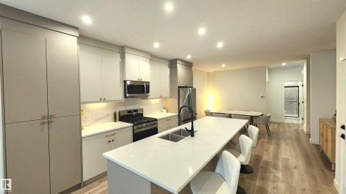 Modern kitchen featuring a large center island with integrated sink, stainless steel appliances, light-toned cabinetry, and recessed lighting - 220 28 Street Sw, Edmonton, AB - Indoor Photo Showing Kitchen With Double Sink With Upgraded Kitchen