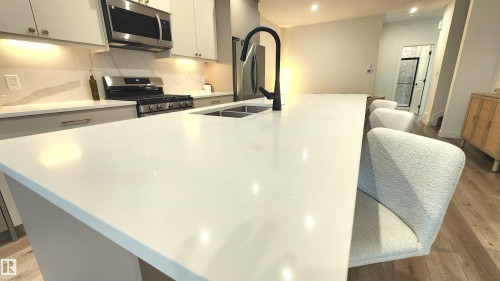 Kitchen featuring a spacious island, stainless steel appliances, dual-basin sink with a matte black faucet, light wood-finish flooring, and light-toned cabinetry - 220 28 Street Sw, Edmonton, AB - Indoor Photo Showing Kitchen With Double Sink With Upgraded Kitchen