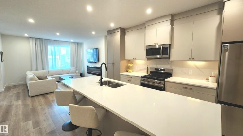Open-concept living area with wood-finish flooring, recessed lighting, and a linear electric fireplace - 220 28 Street Sw, Edmonton, AB - Indoor Photo Showing Kitchen With Double Sink With Upgraded Kitchen