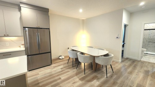 Light wood-finish flooring throughout, stainless steel refrigerator, gray cabinetry with integrated lighting, white countertops and backsplash, and a bathroom with a glass-enclosed shower - 220 28 Street Sw, Edmonton, AB - Indoor