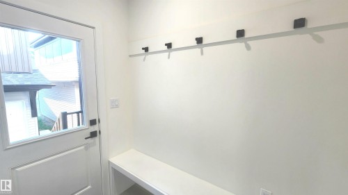 Built-in bench seating with a storage compartment, white interior door with glass panel, matte black door hardware, and a wall-mounted coat rack - 220 28 Street Sw, Edmonton, AB - Indoor Photo Showing Other Room