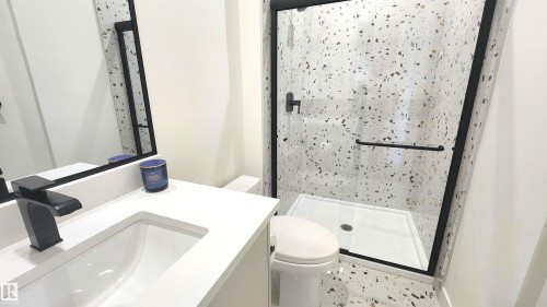 Vanity with integrated sink and matte black faucet, frameless mirror, glass-enclosed shower with matte black hardware, and terrazzo-style wall and floor tiling - 220 28 Street Sw, Edmonton, AB - Indoor Photo Showing Bathroom