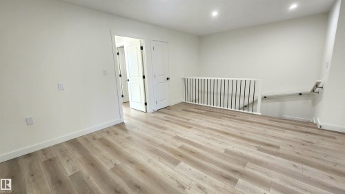 Spacious room featuring wood-finish flooring, recessed lighting, white walls, and contemporary white doors with dark hardware - 220 28 Street Sw, Edmonton, AB - Indoor Photo Showing Other Room