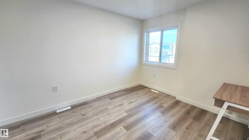 Wood-finish flooring with white baseboards, a white-framed window, and neutral wall paint - 220 28 Street Sw, Edmonton, AB - Indoor Photo Showing Other Room
