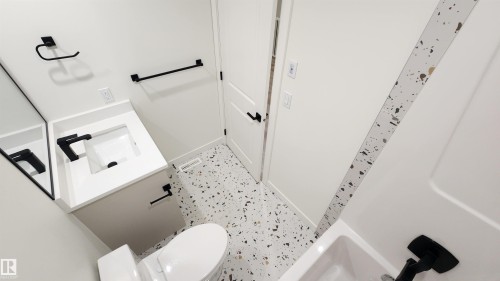 White vanity with integrated sink, black matte fixtures, patterned tile flooring, and a shower/tub combination - 220 28 Street Sw, Edmonton, AB - Indoor