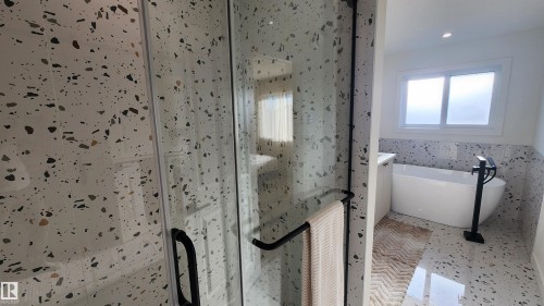 Enclosed shower with black-finish hardware, freestanding soaking tub with black-finish floor-mounted faucet, and a large window with frosted glass - 220 28 Street Sw, Edmonton, AB - Indoor Photo Showing Bathroom
