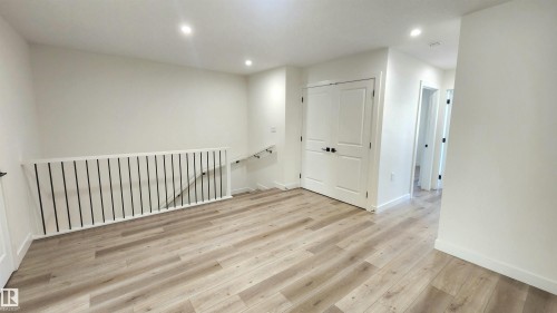 Recessed lighting, wood-finish flooring, white walls, white paneled doors, and a staircase with a white railing and black spindles - 220 28 Street Sw, Edmonton, AB - Indoor Photo Showing Other Room