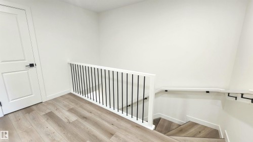 Wood-finish flooring, white walls, white railing with black balusters, white trim, and a white door with black hardware - 220 28 Street Sw, Edmonton, AB - Indoor Photo Showing Other Room
