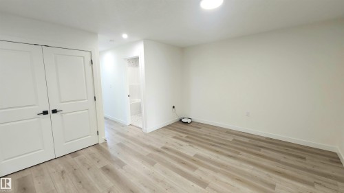 Recessed lighting, light wood-finish flooring, white walls, and white double panel doors with matte black hardware - 220 28 Street Sw, Edmonton, AB - Indoor Photo Showing Other Room