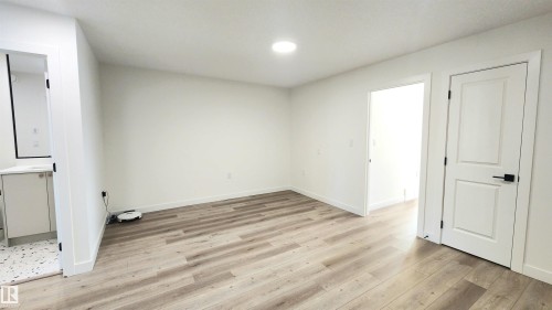 Wood-finish flooring throughout, bright recessed lighting, white walls, and a two-panel interior door with matte black hardware - 220 28 Street Sw, Edmonton, AB - Indoor Photo Showing Other Room