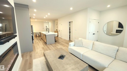 Open-concept living space featuring wood-finish flooring, recessed lighting, a built-in electric fireplace, and a kitchen island with a white countertop - 220 28 Street Sw, Edmonton, AB - Indoor