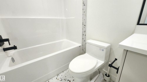 White bathtub with matte black fixtures, modern white toilet, and white vanity with an integrated countertop sink - 220 28 Street Sw, Edmonton, AB - Indoor Photo Showing Bathroom