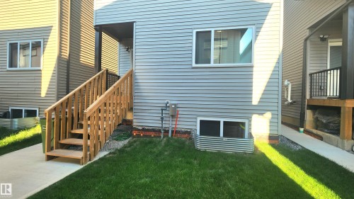 Exterior featuring horizontal vinyl siding, a wooden staircase, a ground-level window well, and a concrete walkway - 220 28 Street Sw, Edmonton, AB - Outdoor With Exterior