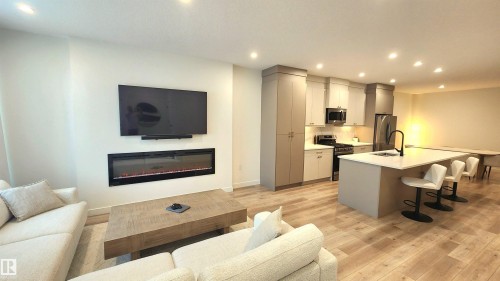 Open-concept living space featuring wood-finish flooring, recessed lighting, and a built-in electric fireplace - 220 28 Street Sw, Edmonton, AB - Indoor With Fireplace