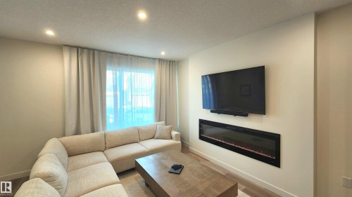 Recessed ceiling lighting, full-height window with sheer and blackout drapery, wall-mounted linear electric fireplace, and wood-finish flooring - 220 28 Street Sw, Edmonton, AB - Indoor Photo Showing Living Room With Fireplace