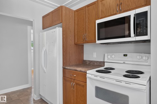 Wood-finish cabinetry, solid surface countertops, white refrigerator, white electric range, and a white microwave - 13214 123 Street Nw, Edmonton, AB 
