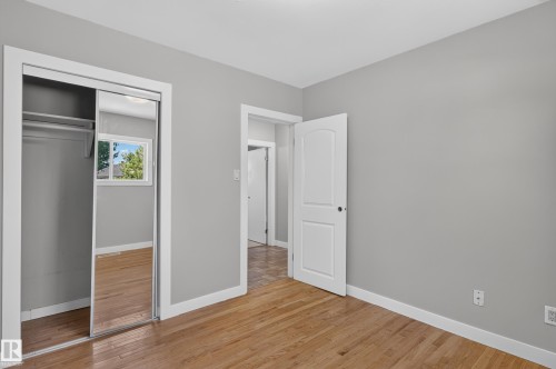Light gray walls, wood-finish flooring, white trim, and a mirrored sliding closet door - 13214 123 Street Nw, Edmonton, AB 