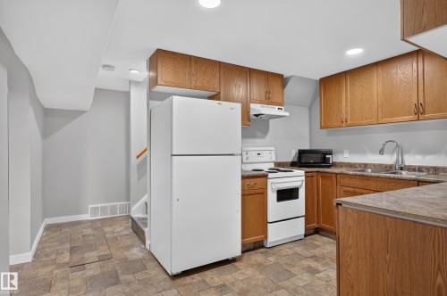 Full kitchen featuring wood-finish cabinetry, a freestanding electric range, and a stainless-steel sink with a gooseneck faucet - 13214 123 Street Nw, Edmonton, AB 
