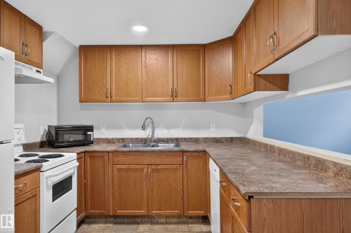 Kitchen featuring wood-finish cabinetry, a double basin sink with a high-arc faucet, and mottled-finish countertops - 13214 123 Street Nw, Edmonton, AB 