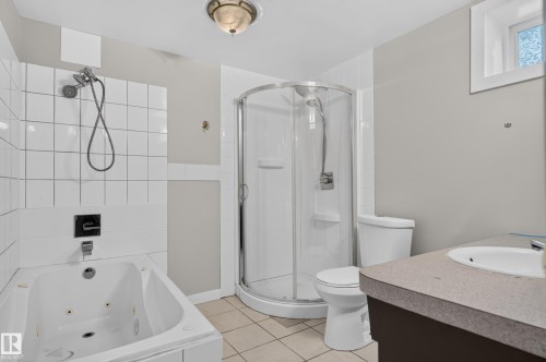 White tiled walls with a built-in jetted tub, a separate glass-enclosed shower, and a single vanity with an integrated sink - 13214 123 Street Nw, Edmonton, AB 