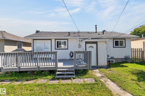 Rear exterior featuring a gray wood-finish deck with railings, dual white French patio doors, and a secondary white exterior door - 13214 123 Street Nw, Edmonton, AB 
