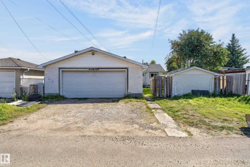 Detached garage with a white overhead door and an additional shed, both featuring stucco exteriors - 13214 123 Street Nw, Edmonton, AB 