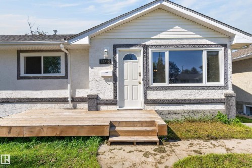 White stucco exterior with dark textured trim accents, front wood deck with steps, prominent front door with arched glass insert, and multiple windows - 13214 123 Street Nw, Edmonton, AB 