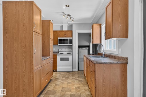 Galley kitchen featuring wood-finish cabinetry, patterned flooring, white appliances, and track lighting - 13214 123 Street Nw, Edmonton, AB 