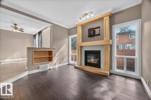 Dark wood-finish flooring, built-in fireplace with a light wood surround, track lighting, dual windows, and an integrated shelving unit - #47 3812 20 Av Nw, Edmonton, AB 