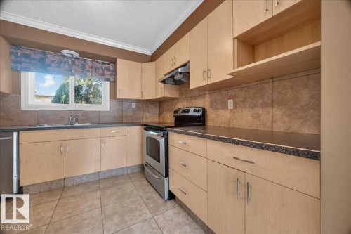 Kitchen with light wood-finish cabinetry, stainless steel appliances, speckled dark countertops, and a tiled backsplash - #47 3812 20 Av Nw, Edmonton, AB 