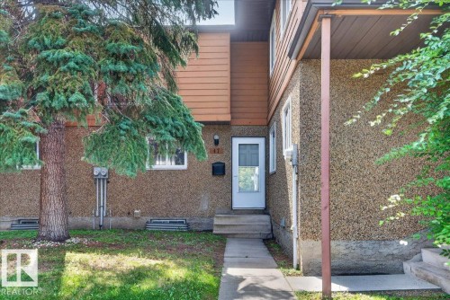 Exterior featuring textured stucco finish, upper-level wood siding, and a prominent evergreen tree - #47 3812 20 Av Nw, Edmonton, AB 